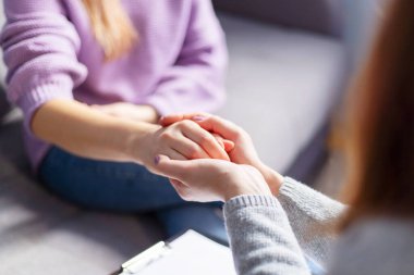 Terapi seansı sırasında bir kadının elini tutan kadın psikoloğun yakın çekimi. Depresyondaki hastasını destekleyen psikoterapist.