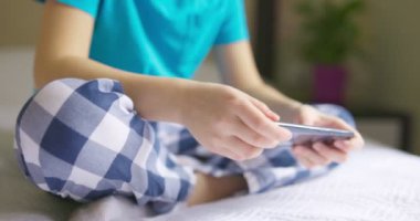 Çocuk akıllı telefon kullanıyor, çocuk internette geziniyor, akıllı telefonla konuşuyor, çocuk yatakta otururken ailesiyle veya arkadaşlarıyla iletişim kuruyor.