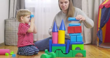 Anne ve oğlu evde yerde oturan renkli küplerle oynuyorlar. Aile, çocuk odasında birlikte vakit geçirir.