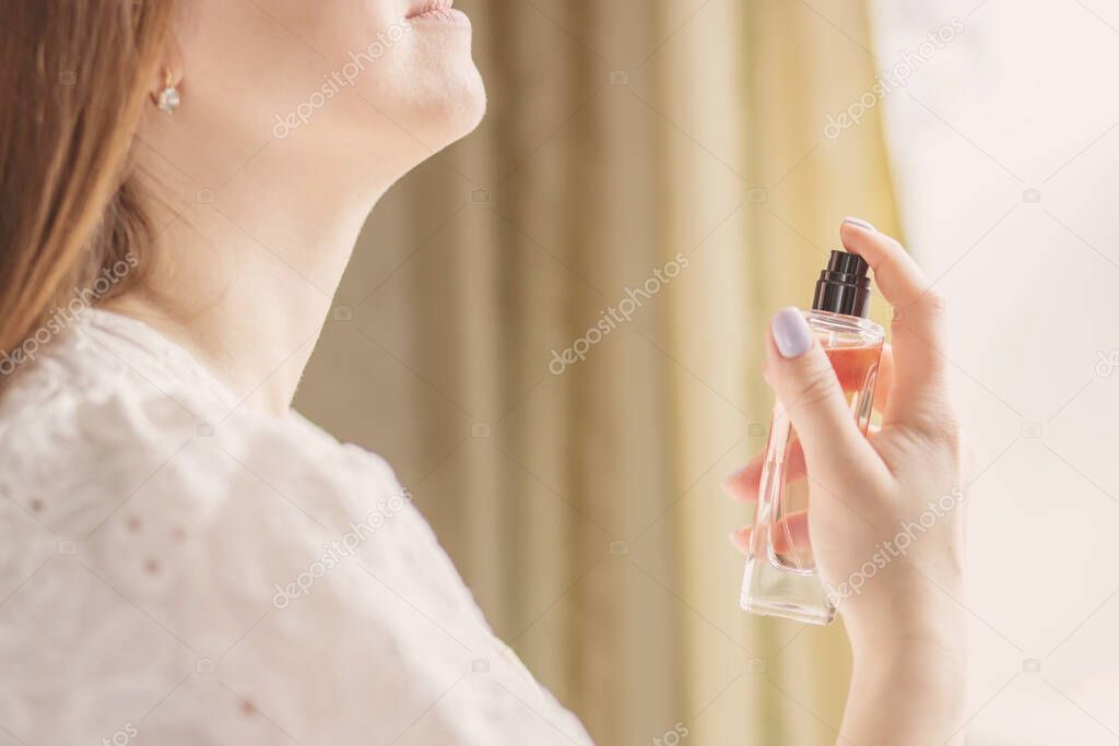 Beautiful young woman holds bottle of perfume and spraying it on neck.