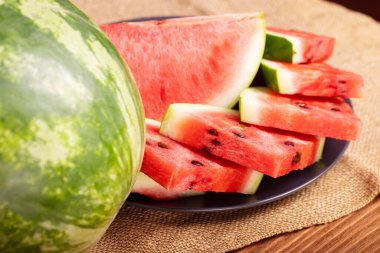 Tahta bir masada siyah bir tabakta taze kırmızı karpuz parçaları. Tatlı ve sulu karpuz.