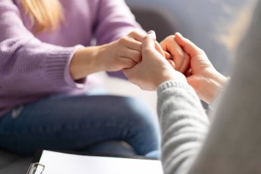 Terapi seansı sırasında bir kadının elini tutan kadın psikoloğun yakın çekimi. Depresyondaki hastasını destekleyen psikoterapist.