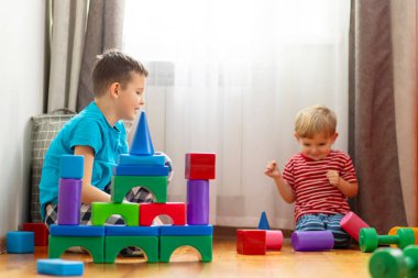 Çocuklar zeminde taş inşa eden çocuklarla oynuyorlar. Küplerden bir kule inşa etmek. Çocuklar için eğitici oyuncaklar.