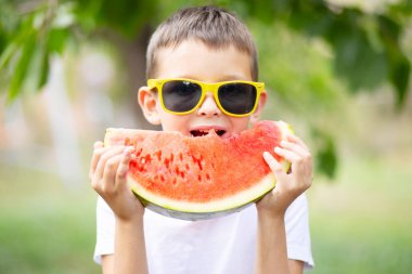 Sarı güneş gözlüklü sevimli çocuk yazın dışarıda karpuz yiyor. Sağlıklı yiyecekler mevsimlik meyve ve meyveler.