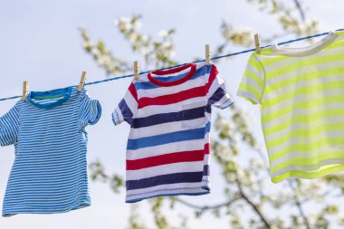 Çamaşır gününde temiz giysiler dışarıda iple asılmış. Mavi gökyüzüne karşı çamaşır ipinde asılı renkli tişörtler.