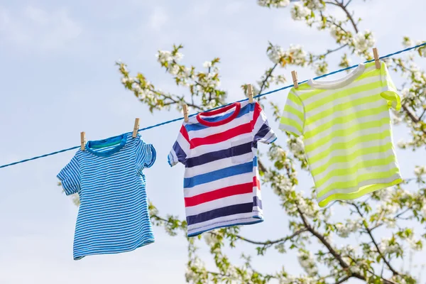 Clean clothes on rope outdoors on laundry day. Colorful t-shirts hanging on a laundry line against blue sky.