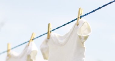 White baby clothes hanging on rope outdoors on spring day.