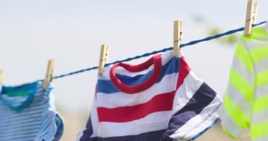 Clean clothes on rope outdoors on laundry day. Colorful t-shirts hanging on a laundry line against blue sky.