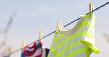 Clean clothes on rope outdoors on laundry day. Colorful t-shirts hanging on a laundry line against blue sky.