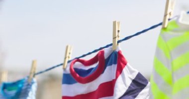 Çamaşır gününde temiz giysiler dışarıda iple asılmış. Mavi gökyüzüne karşı çamaşır ipinde asılı renkli tişörtler.