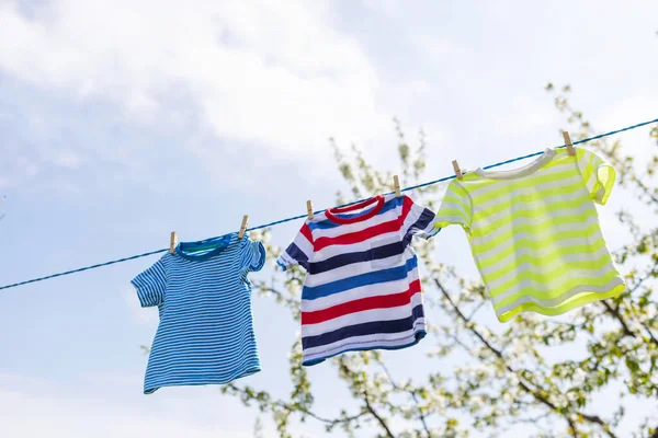 Clean clothes on rope outdoors on laundry day. Colorful t-shirts hanging on a laundry line against blue sky.