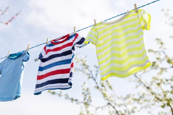 Clean clothes on rope outdoors on laundry day. Colorful t-shirts hanging on a laundry line against blue sky.