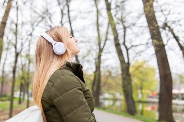 Relaxed woman wearing headphones breathing fresh air listening to music in a park.