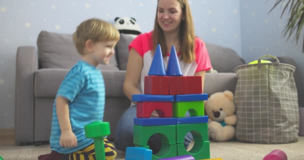 家の床に座っている色のキューブで遊んでいる彼女の息子と母 家族は子供部屋で一緒に家で時間を過ごす — ストック動画