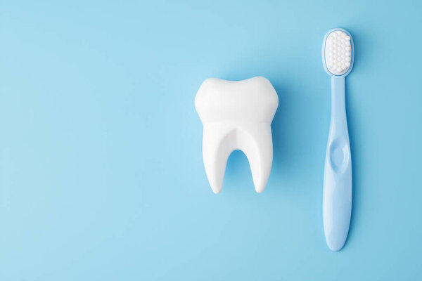 Teeth care and dental hygiene. Toy tooth and toothbrush on blue background, flat lay. Dental concept.