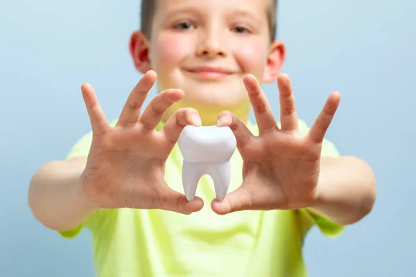 Child holds big tooth on a blue background. Caring for teeth. Dentistry and healthcare concept. Healthy teeth concept.
