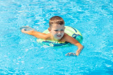 Şişme lastik çemberin üzerinde havuzda yüzen komik çocuk. Çocuk bilardoda oynuyor. Yaz tatili ve tatil konsepti.