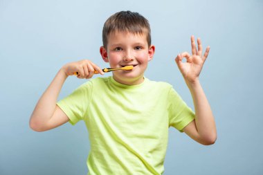 Mutlu çocuk diş fırçasıyla dişlerini fırçalıyor ve mavi arka planda güzel bir jest yapıyor. Sağlık hizmeti, diş hijyeni. Mockup, boşluğu kopyala.