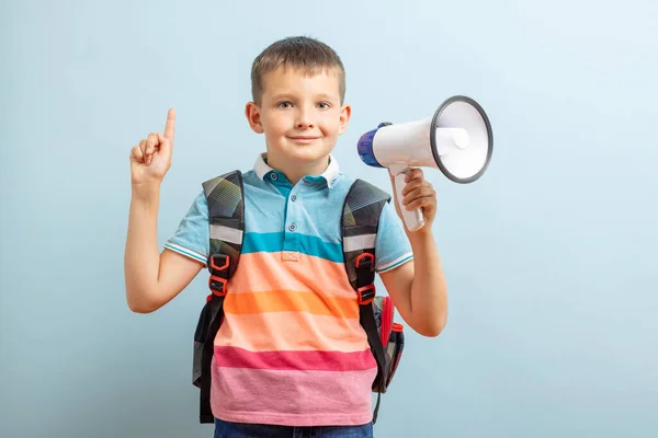 Little schoolboy with megaphone on blue background. Boy with megaphone making an announcement with copy space.