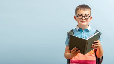 Gözlüklü küçük okul çocuğu mavi arka plan hakkında bir kitap okuyor. Eğitim ve okul konsepti. Mockup, boşluğu kopyala