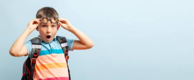 Mavi arka planda sırt çantası olan gözlüklü bir öğrenci. Okula dönelim. Mockup, boşluğu kopyala.