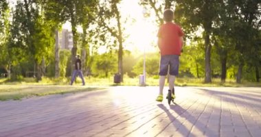 Child with kick scooter. Young boy riding on scooter on path in the park in summer. Kids leisure activity, sport