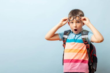 Mavi arka planda sırt çantası olan gözlüklü bir öğrenci. Okula dönelim. Mockup, boşluğu kopyala.