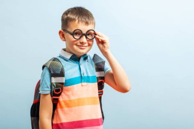 Happy smiling schoolboy in glasses with backpack on blue background. School concept. Back to school.