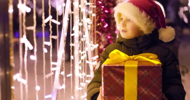 Noel Baba Şapkalı Çocuk Noel Işıklarının Yanında Hediye Kutusuyla Noel — Stok video