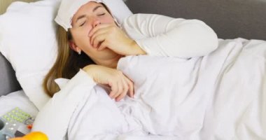 Sick young woman sick with severe cough lying in bed under the blanket at home.