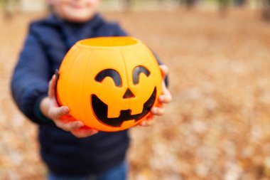 Çocuğun elinde sonbahar parkında Cadılar Bayramı balkabağı şeklinde bir kova var. Balkabağı fenerli çocuk. Cadılar Bayramı - Geleneksel Amerikan bayramı.