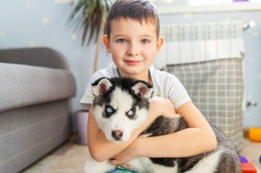 Şirin çocuk evde yerde oturan Sibirya köpeği köpeğine sarılıyor. Aşk ve evcil hayvanlar.