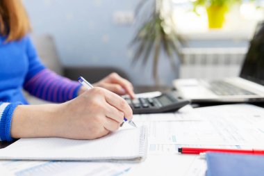 Woman using using calculator for calculate home finances or car taxes, woman managing home family expenses using calculator, making payment on laptop.