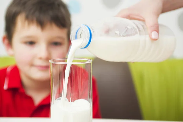 Mother is pouring milk from jar into glass for her son in kitchen. Favorite morning drink.