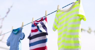 Clean clothes on rope outdoors on laundry day. Colorful t-shirts hanging on a laundry line against blue sky