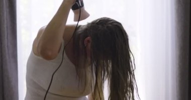 Evdeki pencerenin yanında saç kurutma makinesi kullanan güzel bir kadın.