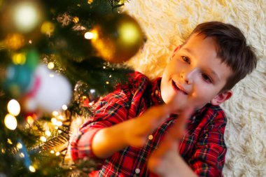 Little cute child decorating the Christmas tree on Christmas Eve at home.