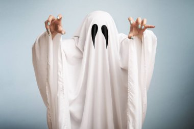 Halloween Concept. A white ghost with black eyes, made from a bedsheet on blue background.