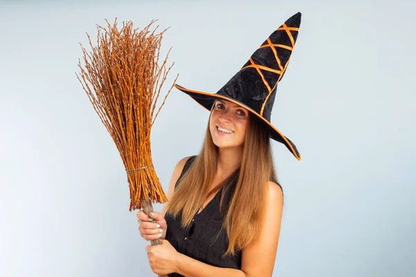 Happy Halloween! Happy young woman in halloween witch costume with broom on a light background. Halloween party concept.
