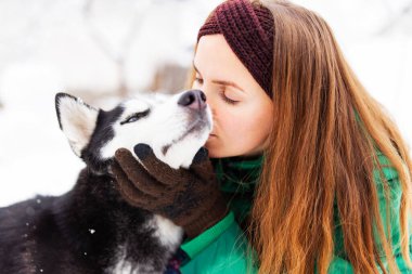 Güzel bir kadın köpeğiyle oynuyor. Kışın açık havada mavi gözlü siyah beyaz kurt köpeğiyle.