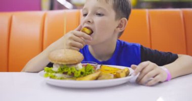 Fast food restoranında hamburger ve patates kızartması yiyen bir çocuk. Kızarmış cipsi domates sosuna batıran bir çocuk. Yüksek kalite 4k görüntü