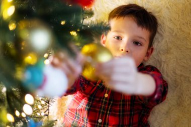 Little cute child decorating the Christmas tree on Christmas Eve at home.