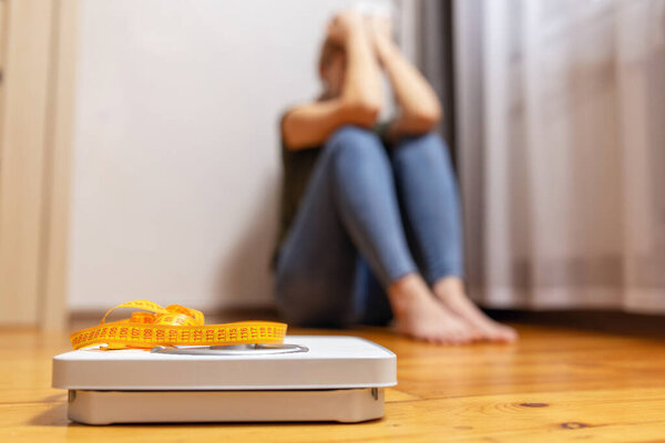 White scale and depression, upset and sad woman with measuring tape on wooden floor.