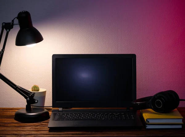 Laptop, kulaklık, masa lambası, defter, telefon ve çiçek. Karantinada mesafeli çalışma kavramı. Modern serbest çalışma. Mesafe iletişimi. Akşamları çalış..