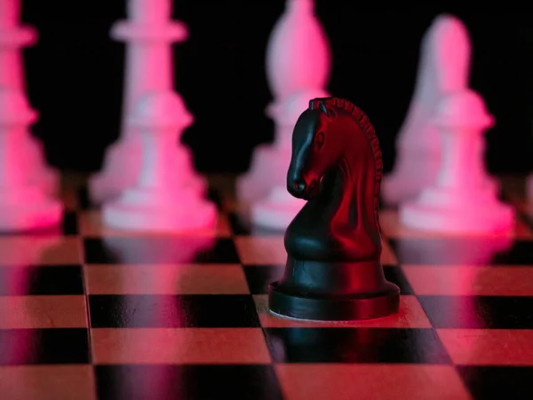 Black horse chess piece on a chessboard. Chess match. Bright red light. Acid colors. The concept of a successful team work leader. Business strategy.