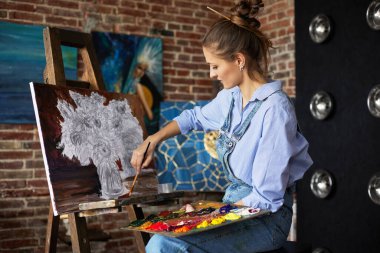 Genç ve güzel kadın ressam, yağlı boya tabloları ve sanat fırçasıyla tuval üzerinde ayçiçeğiyle resim yapıyor. Ressam sanat stüdyosunda sanat eseri yaratıyor. Rahatlama, rahatlama, hobi, stres yönetimi