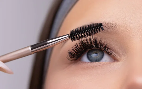 Kadın yüzünün yakın portresi. Taze, yumuşak tenli, uzun siyah kirpiklerini özel rimel fırçasıyla tarayan genç ve güzel bir kız. Sahte kirpikler. Kirpikleri kapat.