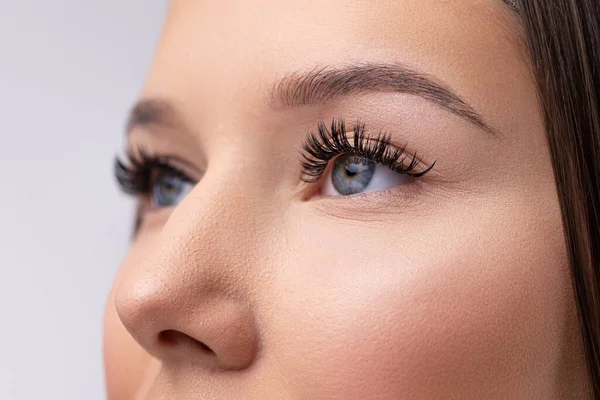 Närbild av kvinnans ansikte. Ung, vacker tjej med fräsch mjuk hud som kammar långa svarta ögonfransar med speciell mascara borste. Falska ögonfransar. Ögonfransar förlängningar närbild — Stockfoto