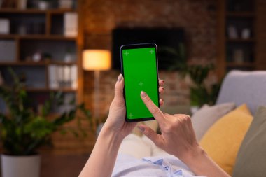 Omuz hizasında elinde yeşil model ekran modu olan akıllı telefon tutan genç bir kadın. Akşam evde kanepede uzanmış içerik video blogları, haberler veya filmler seyreden bir kadın.