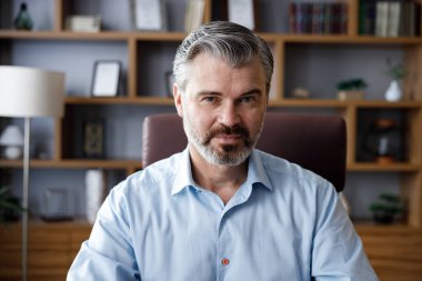 Kendine güvenen yakışıklı iş adamının iş portresi kameraya bakıyor ve gülümsüyor. Beyaz saçlı, kapalı bir ofiste beyaz bir adamın ön kapak portresi. İnsan yüzü